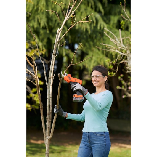 Photography of BLACKDECKER BCPP18D1 cordless pruner used for cutting tree branches outdoors.