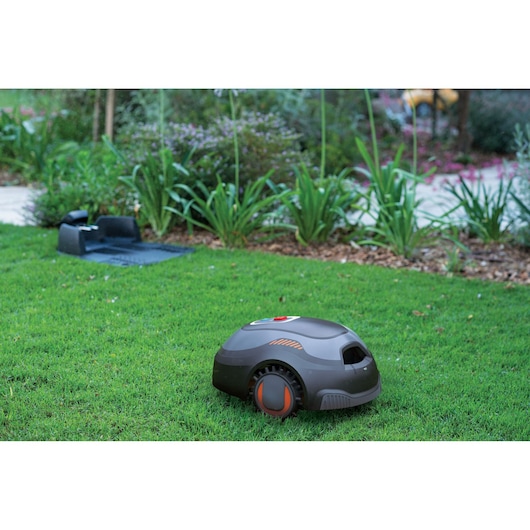 BLACKDECKER BCRMW121 robotic lawn mower on grass near charging station, outdoor angle.