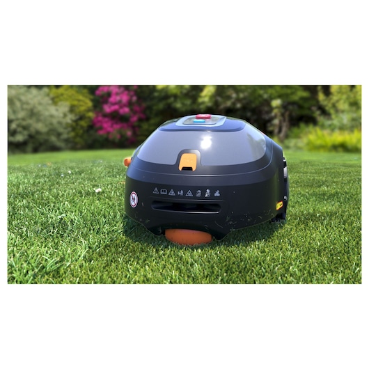 BLACKDECKER BCRMW123 robotic lawn mower on grass, side angle, black body with orange accents and control buttons.