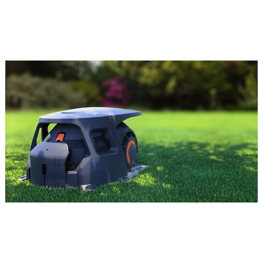 BLACKDECKER BCRMW123 robotic lawn mower with dark grey body and orange accents on grass outdoors.
