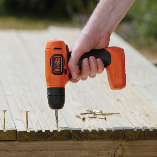 Photo of BLACKDECKER BDCD8K cordless drill driving a screw into wooden planks outdoors.