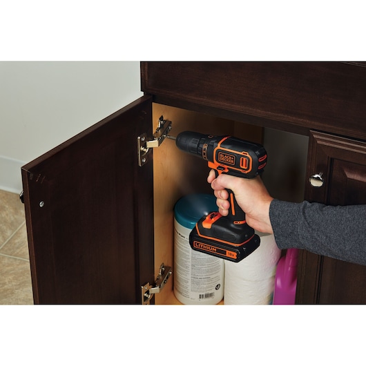 Photo of BLACKDECKER BDCDC18BTA cordless drill in use fixing a cabinet hinge in a kitchen setting.