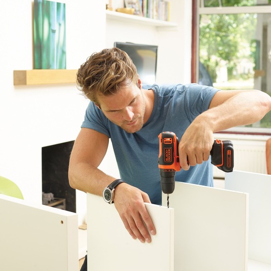 Photo of BLACKDECKER BDCDD12K1B cordless drill used for assembling white furniture indoors.