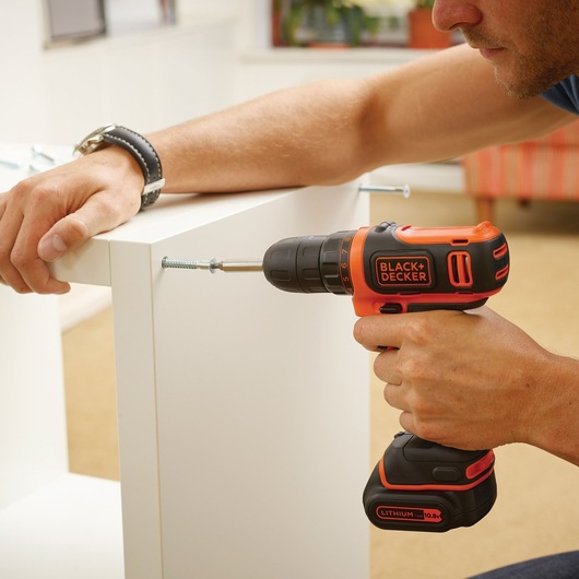 BLACKDECKER BDCDD12K1B cordless drill used to assemble white furniture indoors.
