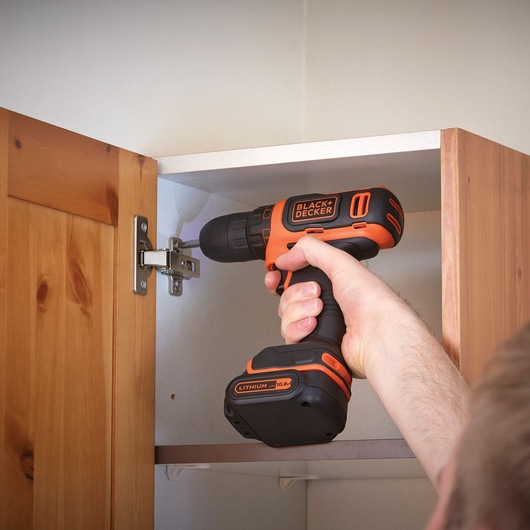 BLACKDECKER BDCDD12K1B cordless drill used to install cabinet hardware, orange and black, close-up.