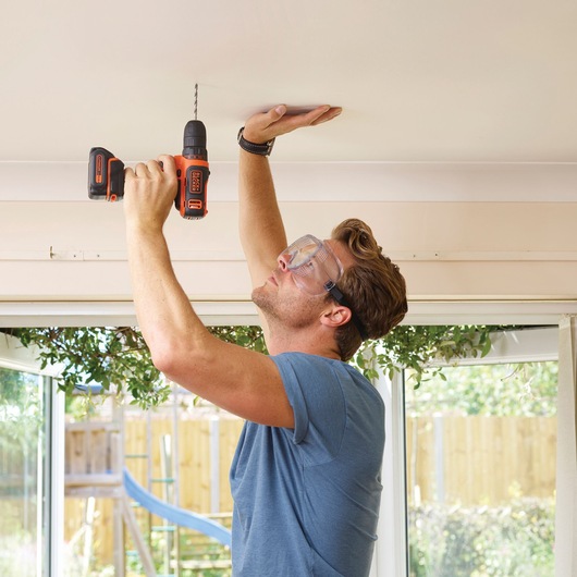 Photo of person using BLACKDECKER BDCDD12K1B cordless drill to drill into indoor ceiling.