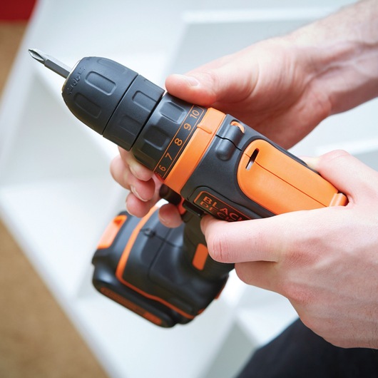Photo of BLACK+DECKER BDCDD12K1B cordless drill driver held in hands, orange and black color, with visible torque settings.