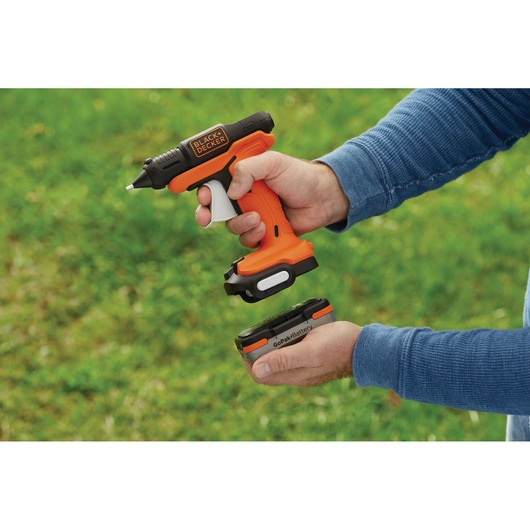 Photo of BLACK+DECKER BDCGG12N cordless glue gun with orange and black design, person attaching GoPak battery outdoors.