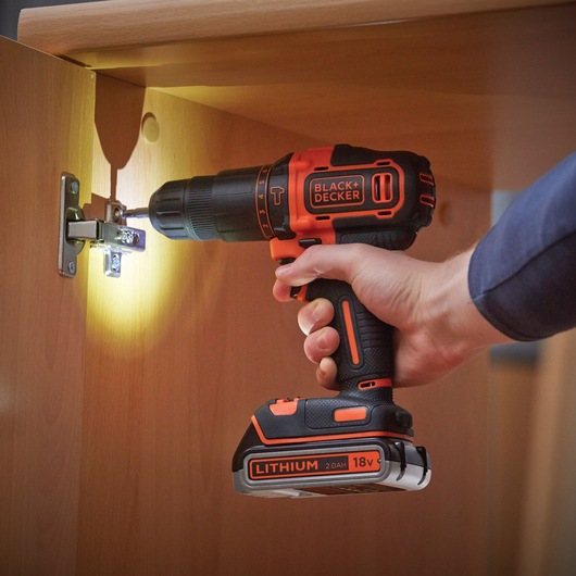 BLACKDECKER BDCHD18K1B2 cordless drill used on cabinet hinge, orange and black, 18V lithium battery.