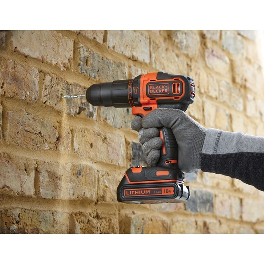 BLACKDECKER BDCHD18KB2 cordless drill in use drilling into brick wall, close side view.