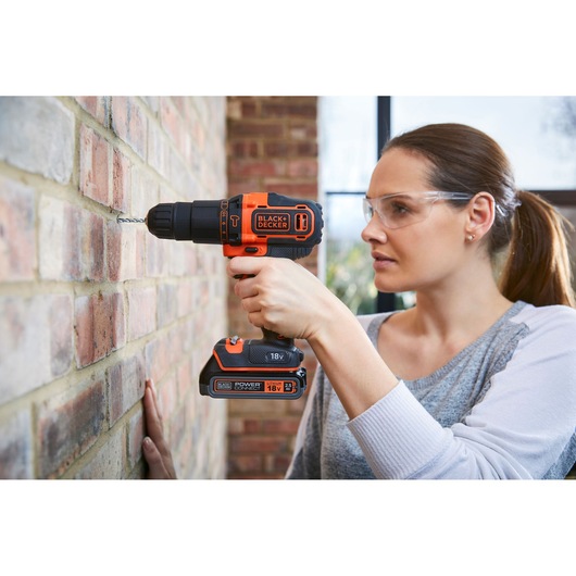 Photo of BLACKDECKER BDCHD18KB cordless drill used to drill into a brick wall, held by a person indoors.