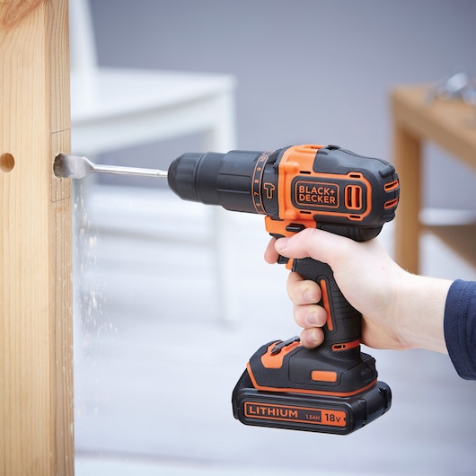 Black+Decker BDCHD18K cordless drill being used to drill into wood, side view, orange and black design.