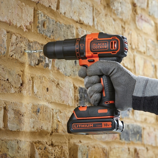 BLACK+DECKER BDCHD18K cordless drill in use on brick wall, orange and black, photography close-up.
