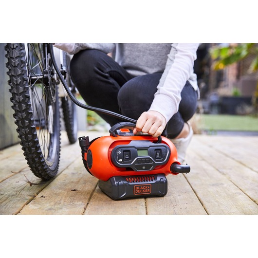 BLACKDECKER BDCINF18N portable air compressor inflating bicycle tire outdoors on wooden deck.
