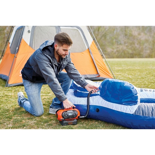 BLACKDECKER BDCINF18N portable air inflator being used to inflate a blue air mattress outdoors near an orange tent.