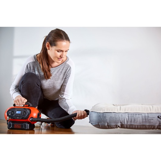 BLACK+DECKER BDCINF18N portable inflator being used to inflate an air mattress indoors.