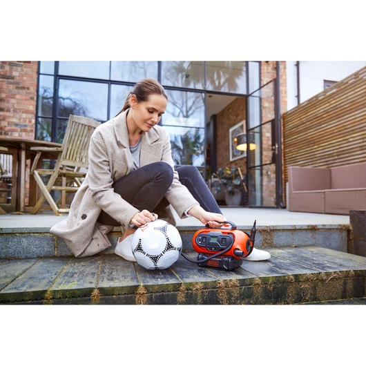 BLACKDECKER BDCINF18N inflator being used outdoors to inflate a soccer ball, woman sitting on garden steps.