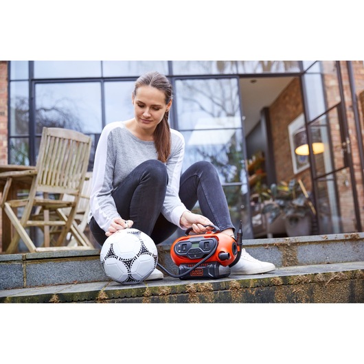 BLACK+DECKER BDCINF18N inflator used outdoors to inflate a white soccer ball, person sitting on steps.