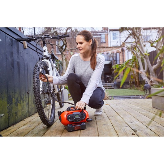 Photo of BLACKDECKER BDCINF18N portable inflator being used to inflate a bicycle tire outdoors.