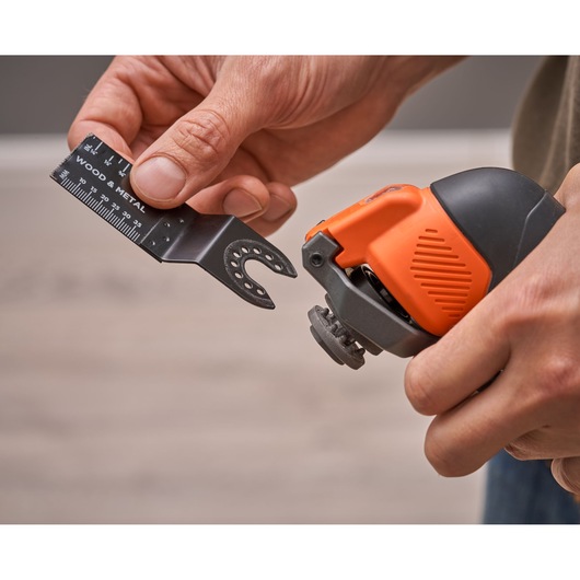 Close-up photo of BLACKDECKER BDCOS18D1K multi-tool with orange and black handle, user attaching a saw blade.