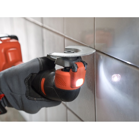 BLACKDECKER BDCOS18N oscillating multi-tool in use cutting tile grout, close-up angle, LED light on.