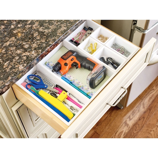 BLACK+DECKER BDCSFS30C cordless screwdriver in orange and black stored in a kitchen drawer with office supplies, top view.