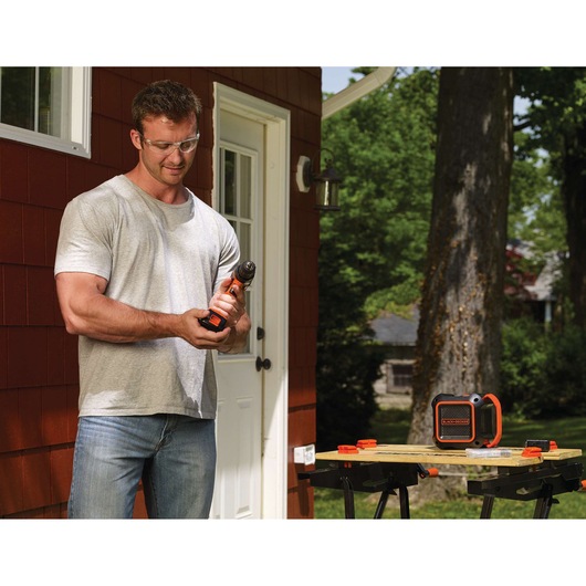 Photo of BLACKDECKER BDCSP18N portable speaker on a workbench outside near a man holding a power tool.