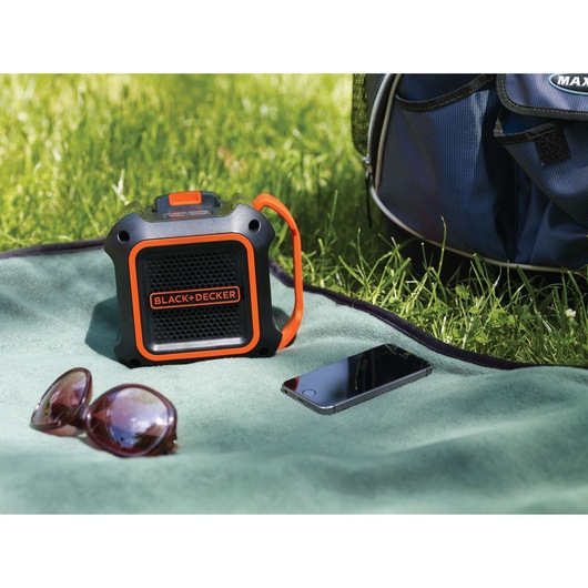 BLACKDECKER BDCSP18N portable speaker with orange trim on a picnic blanket outdoors.