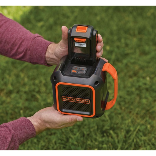 Photo of BLACK+DECKER BDCSP18N portable outdoor speaker with battery inserted, shown in use on grass.