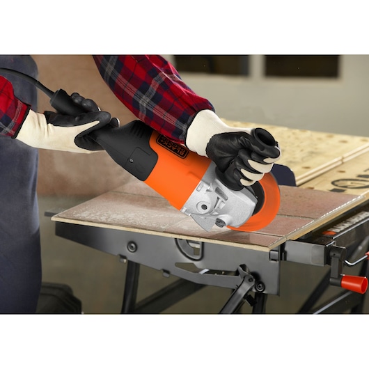 BLACK+DECKER BDGL2223 angle grinder in use, cutting tile on workbench, close-up view.