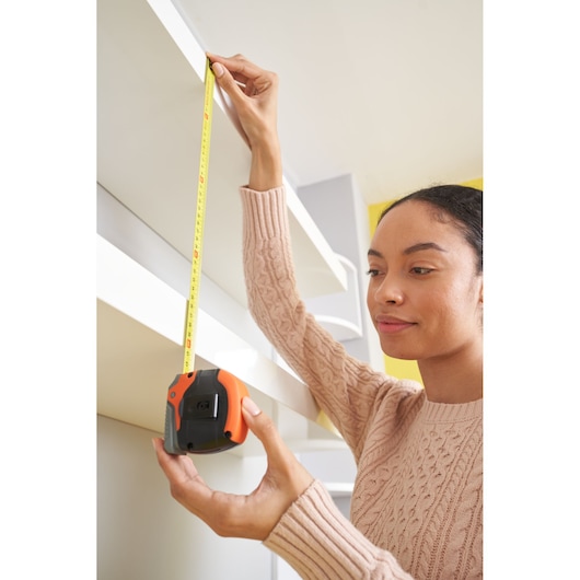 Person using BLACKDECKER BDHT84002 tape measure to measure white shelf height.