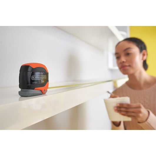 BLACKDECKER BDHT84002 tape measure with black and orange casing extended on white shelf.
