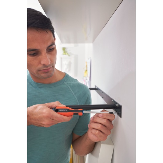 BLACKDECKER BDHT84014 screwdriver used to assemble metal bracket on wall, orange handle, close-up.