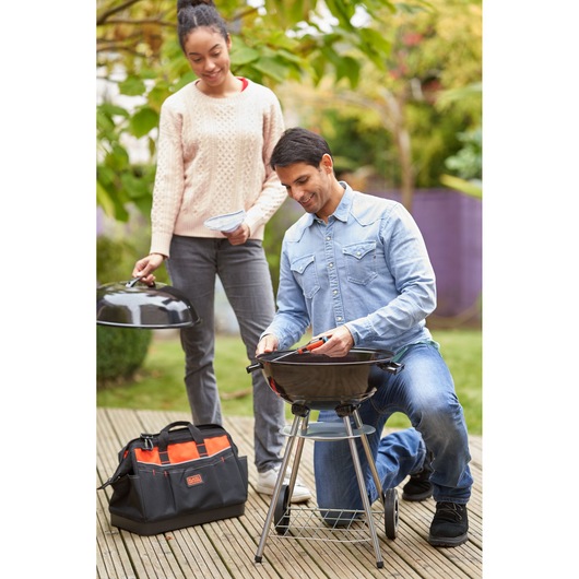 BLACKDECKER BDHT84014 tool bag on deck beside people preparing a barbecue outdoors.