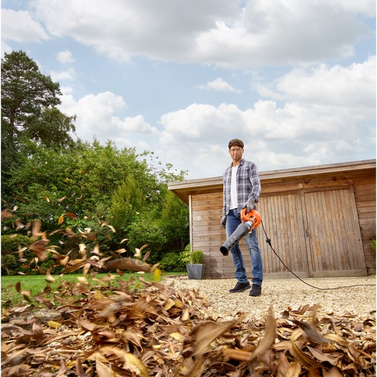 BLACKDECKER BEBL185 leaf blower in use outdoors, orange and black color, leaves blowing on gravel.