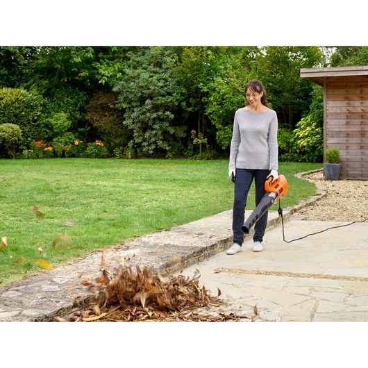 BLACKDECKER BEBL185 leaf blower in use clearing leaves on patio in garden setting.