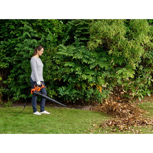 BLACKDECKER BEBLV301 leaf blower held by person clearing leaves outdoors near bushes.