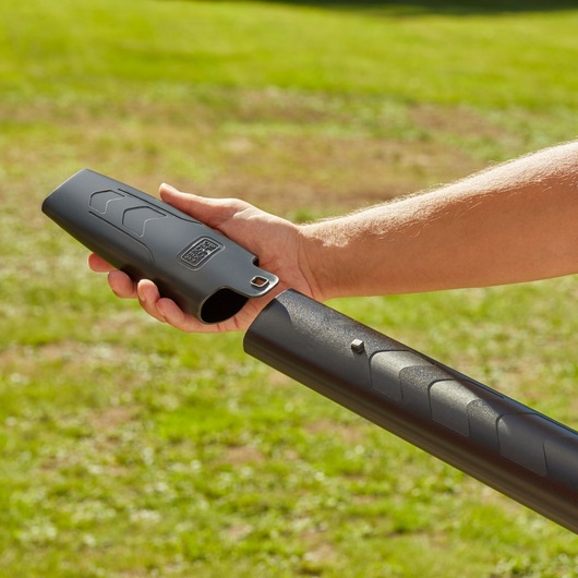 Photo of BLACK+DECKER BEBLV301 leaf blower tube attachment in a hand, shown outdoors on grass.
