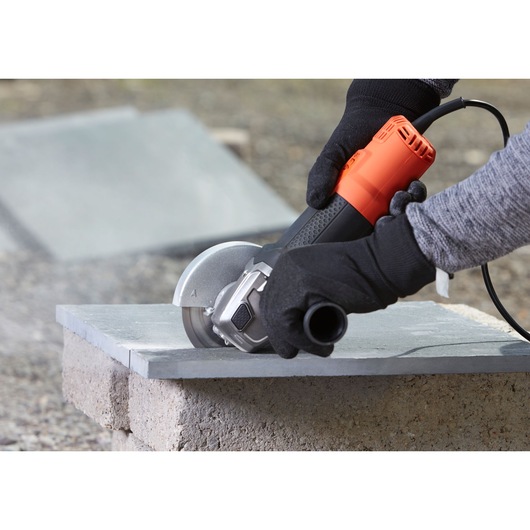 BLACKDECKER BEG220 angle grinder cutting stone slab outdoors, person wearing black gloves.