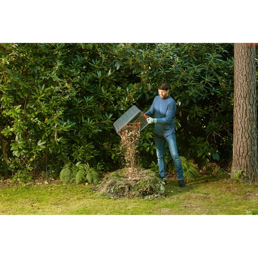 BLACKDECKER BEGAS5800 garden shredder, person emptying shredded material onto a compost pile outdoors.