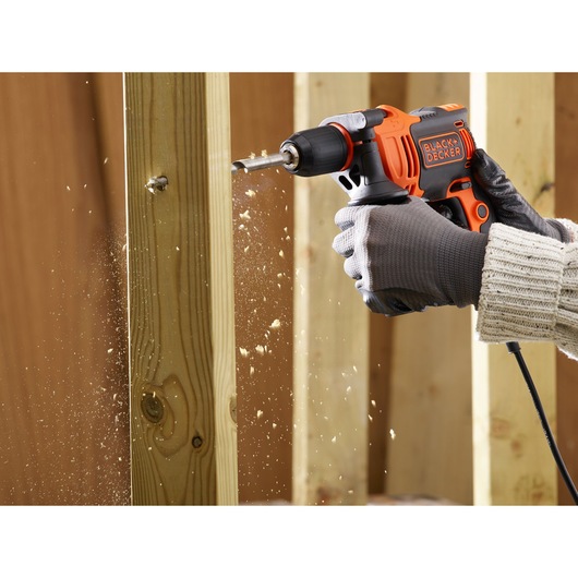 Photo of BLACK+DECKER BEH710K corded drill in use drilling into wooden beam, wood shavings flying.
