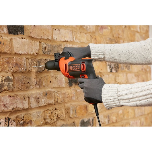 BLACKDECKER BEH710K corded hammer drill in use drilling into a brick wall, close-up side angle.