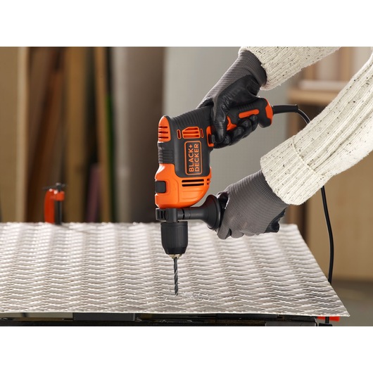 BLACKDECKER BEH710K hammer drill in use, drilling into metal sheet, person wearing gloves.