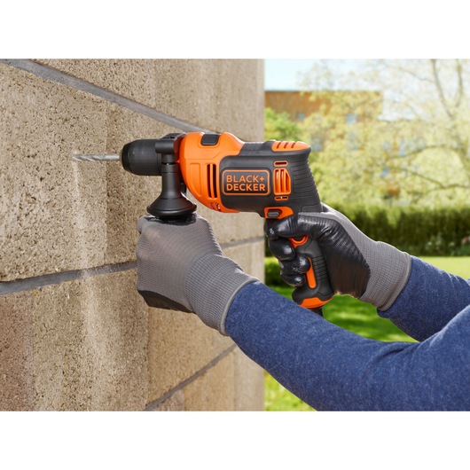 BLACK+DECKER BEH710K hammer drill in use drilling into concrete wall, orange and black design.