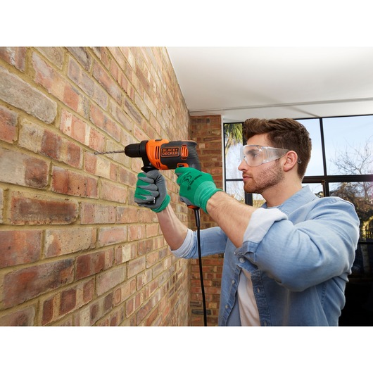 BLACK+DECKER BEH710K hammer drill used on brick wall, orange and black design, photography scene.