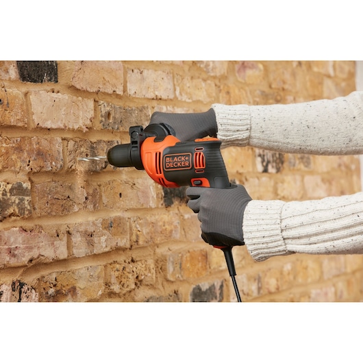 BLACK+DECKER BEH710SA32 hammer drill in use on a brick wall, close-up side view.