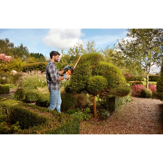 BLACKDECKER BEHTS301 hedge trimmer in use trimming topiary in a garden.