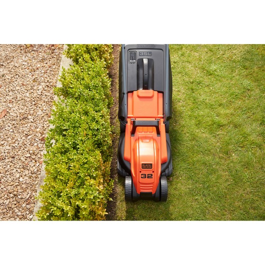 BLACK+DECKER BEMW451BH lawn mower top view cutting grass next to hedge and gravel path.