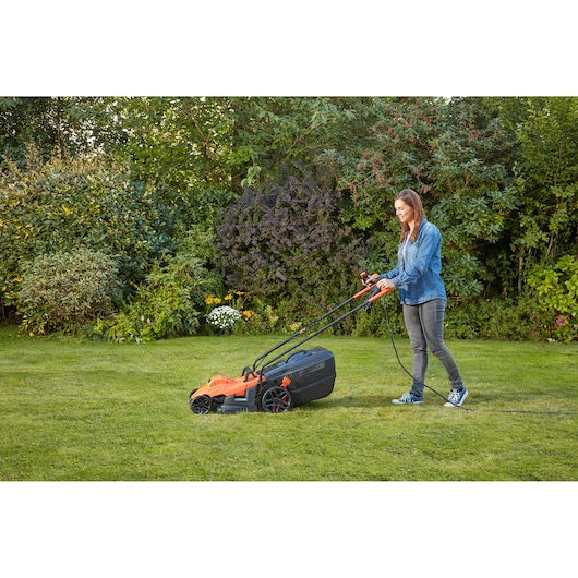 Person using BLACKDECKER BEMW461BH electric lawn mower on green grass in garden.
