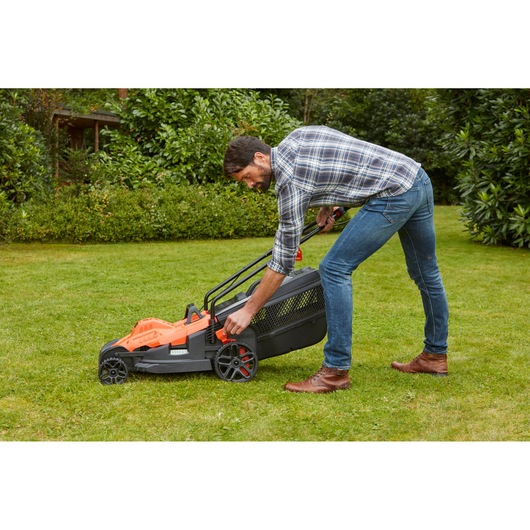 BLACKDECKER BEMW461BH lawn mower with orange and black body, user adjusting height on grass.